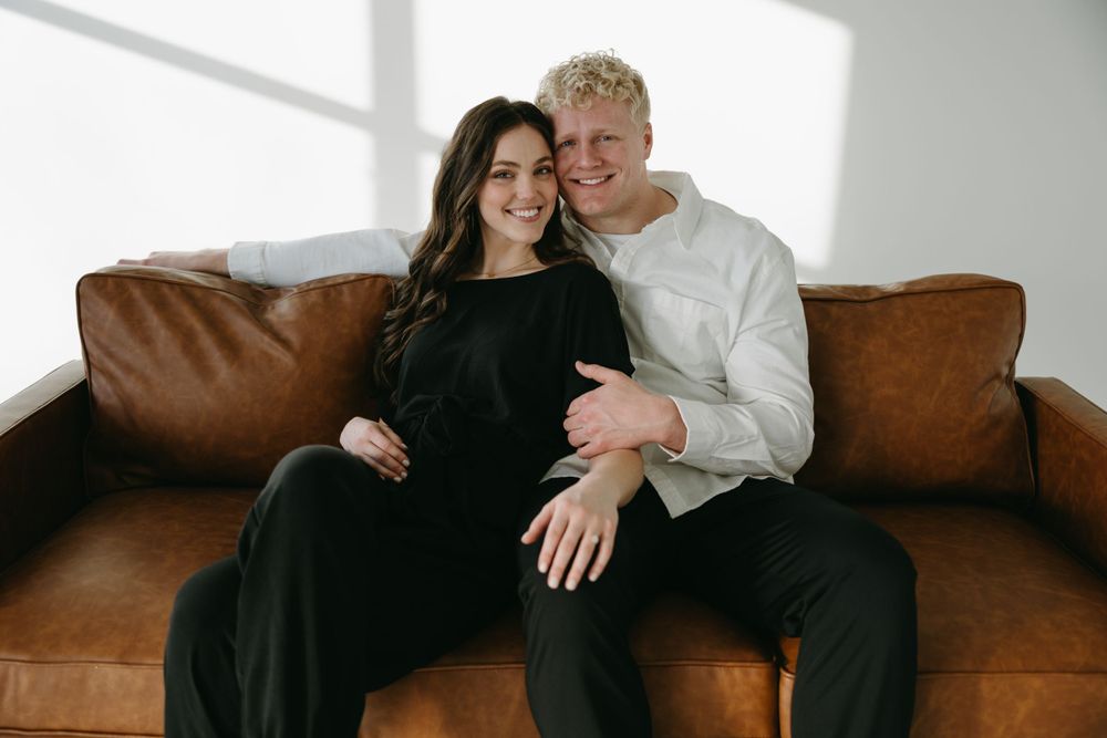 A tender moment shared between a couple relaxing on a brown leather couch in a bright contemporary setting.