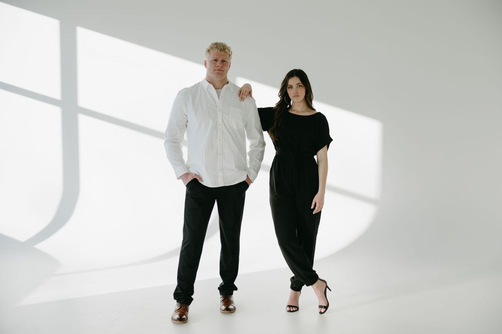 An elegant couple poses together in a minimalist white studio setting wearing coordinated black and white outfits.