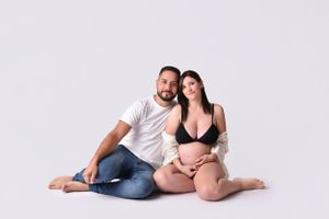 A maternity photo shoot on a light background with casual styling.