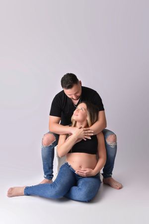 Tender maternity pose with couple in casual denim and black against neutral backdrop.
