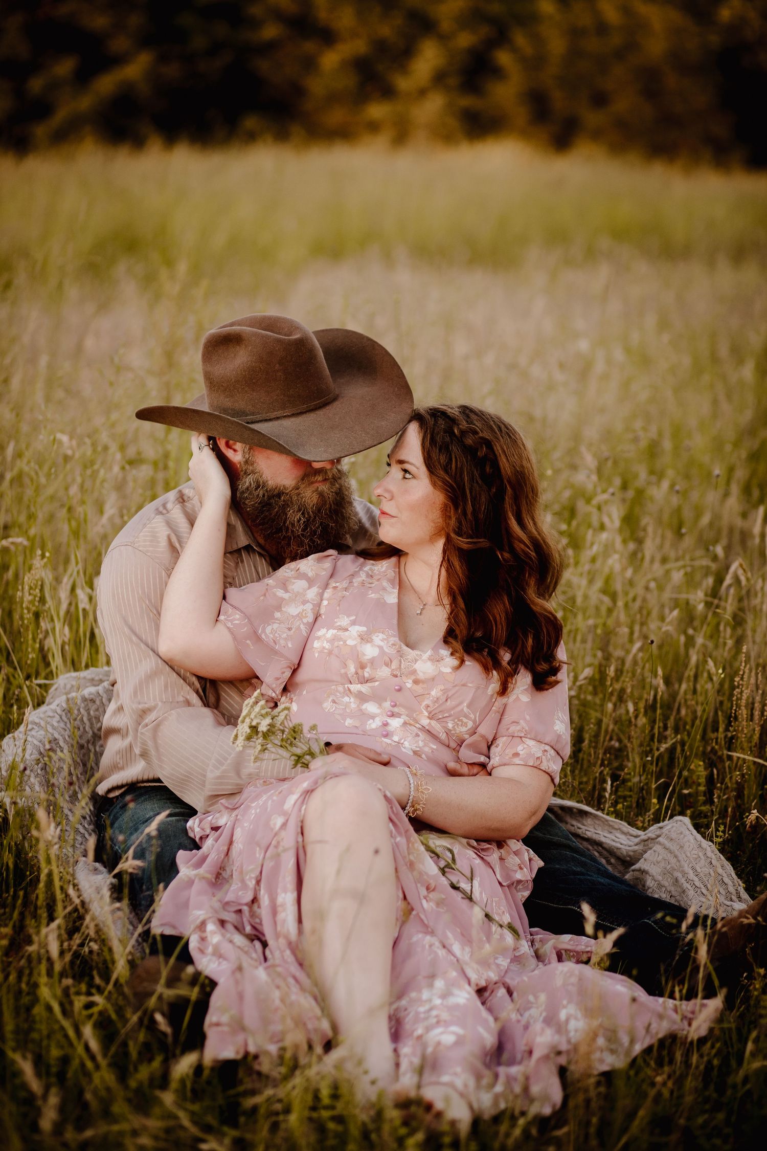 Couple in romantic embrace lying in tall grass field at golden hour.