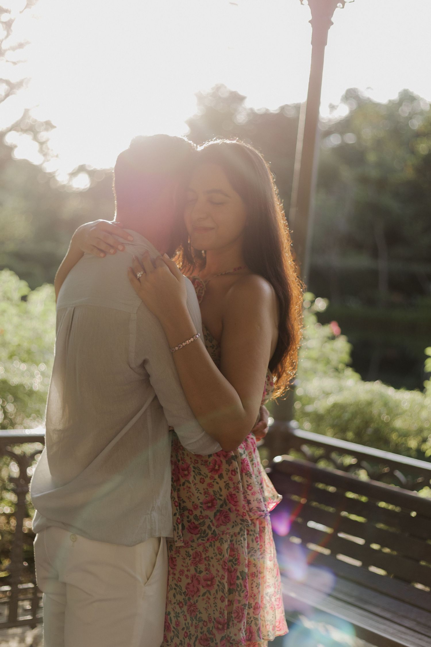Playful couple poses on grass during outdoor photoshoot with floral dress and casual wear.