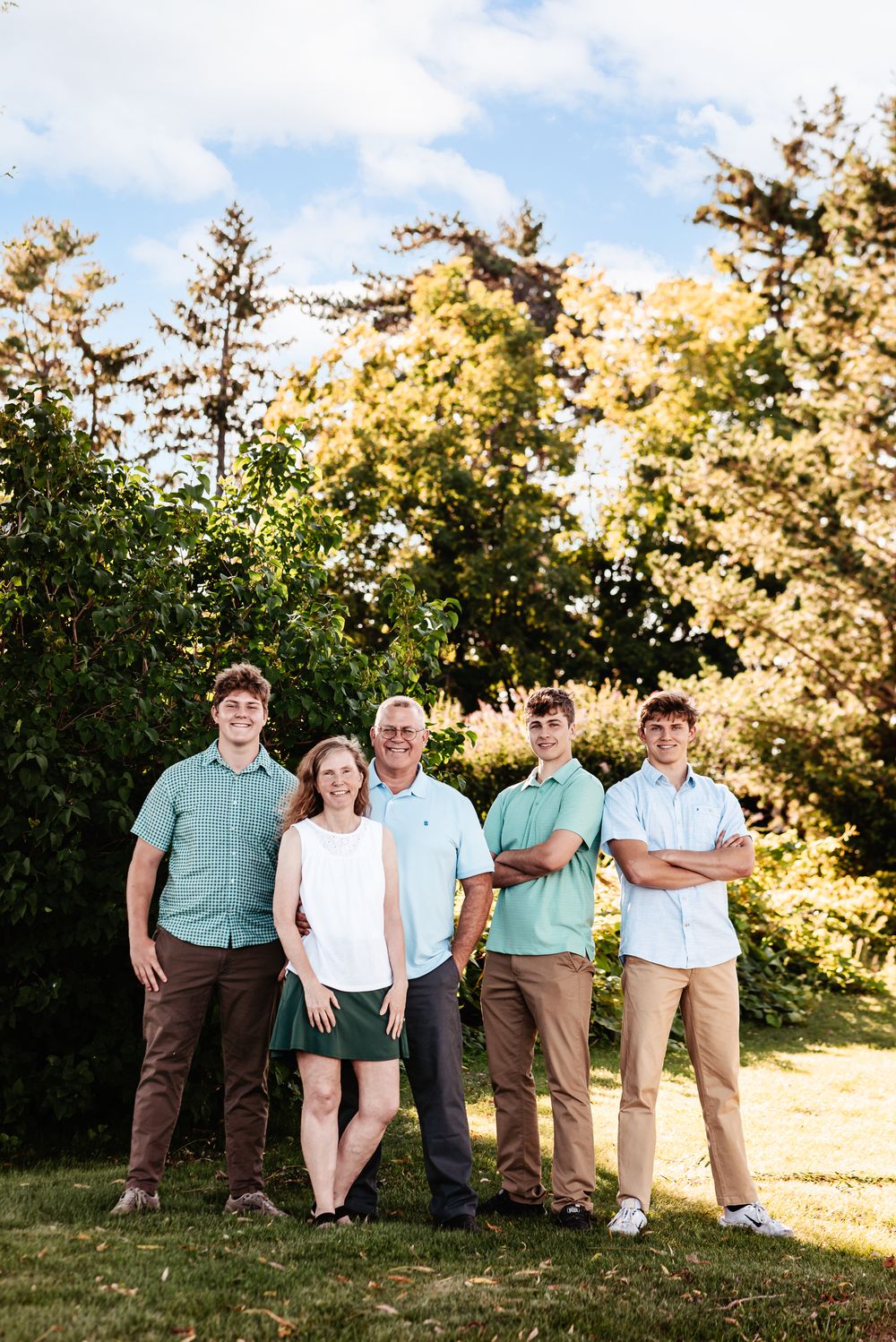 A family poses casually on a grassy hill during golden hour with trees in the background.