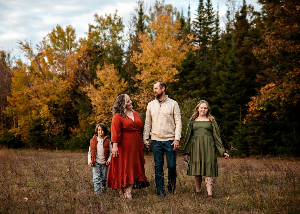 A group of people walking together through a scenic autumn field with golden trees in the background.