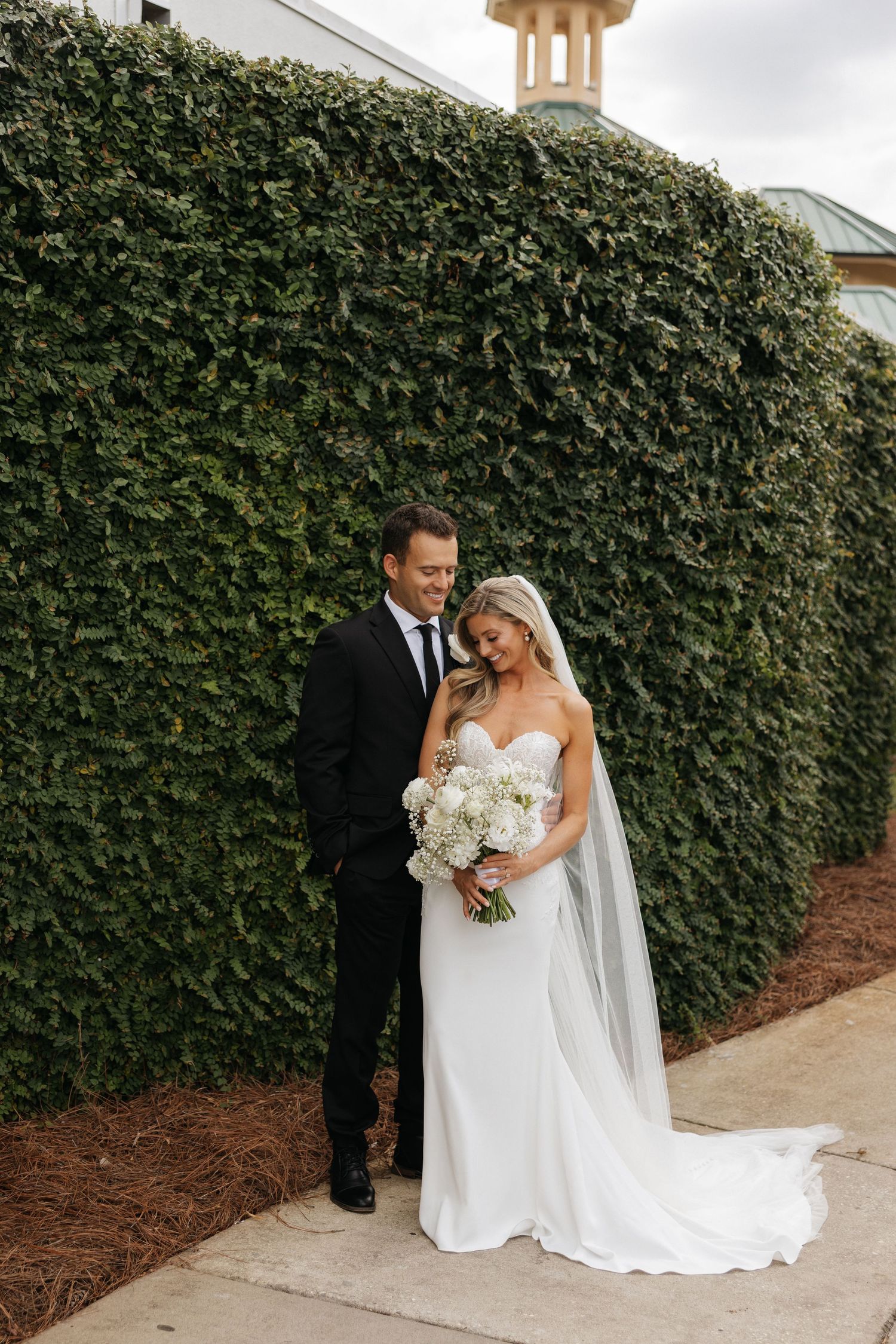 Romantic outdoor wedding portrait at sunset with couple embracing on grassy lawn as bride holds eucalyptus bouquet. Eden Gardens in 30A