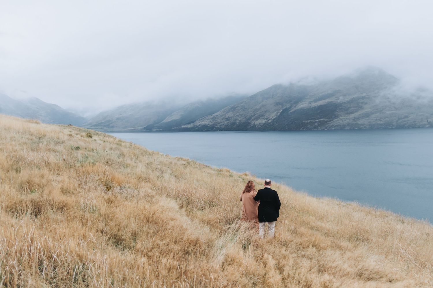 Photographer captures misty landscape from golden hillside overlooking serene mountain lake.