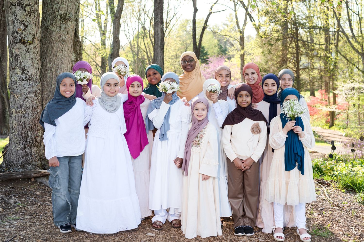 Group of girls wearing colorful hijabs and modest dresses posing together outdoors in a park setting.