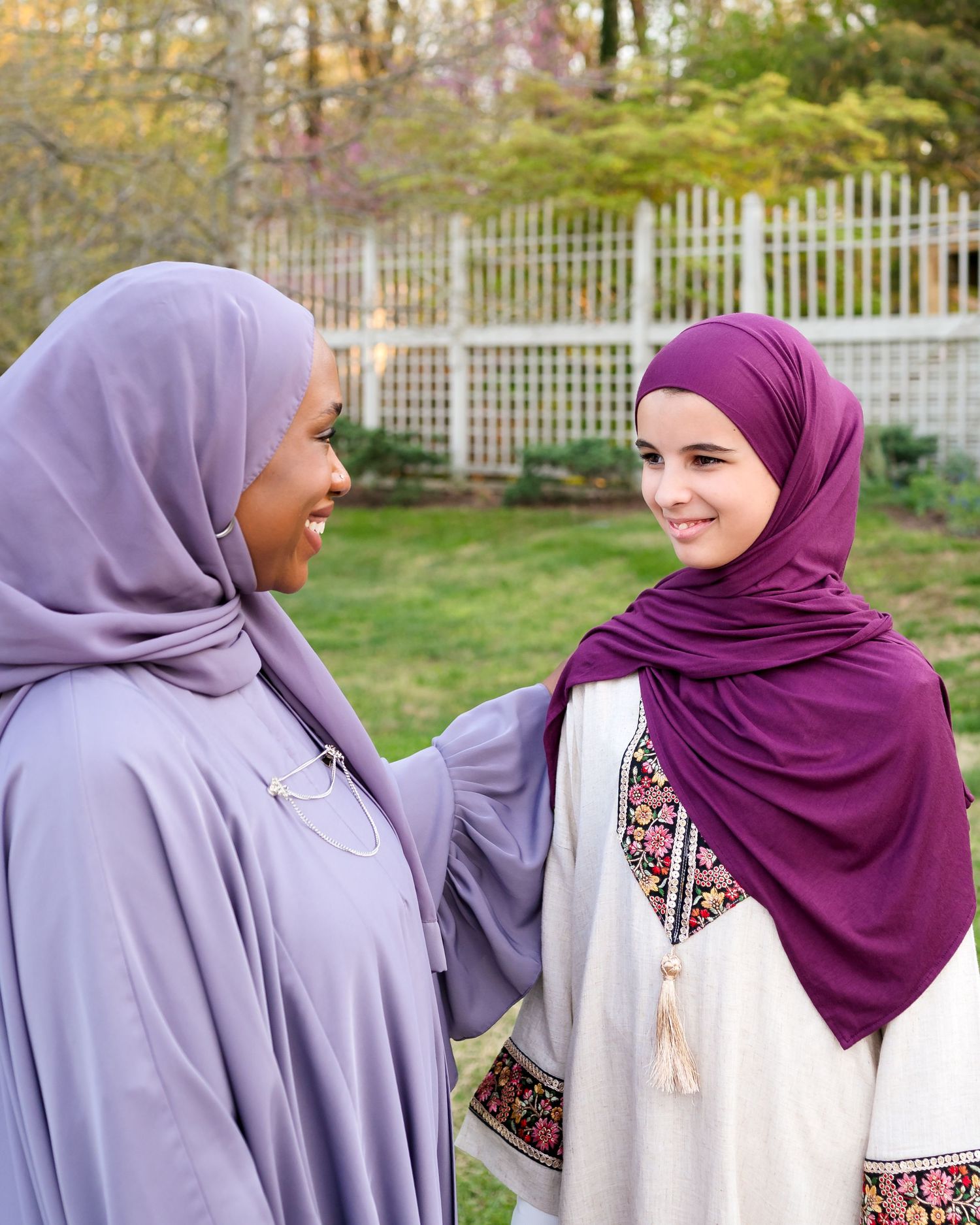Two women in colorful hijabs smiling at each other outdoors.