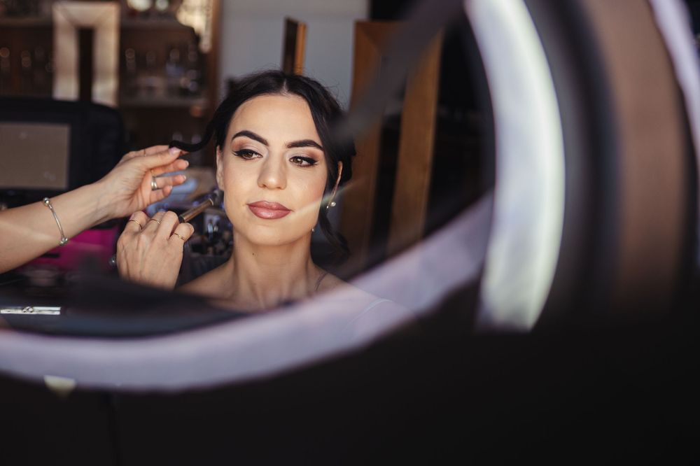Makeup artist applies cosmetics while working with professional ring light in beauty studio.