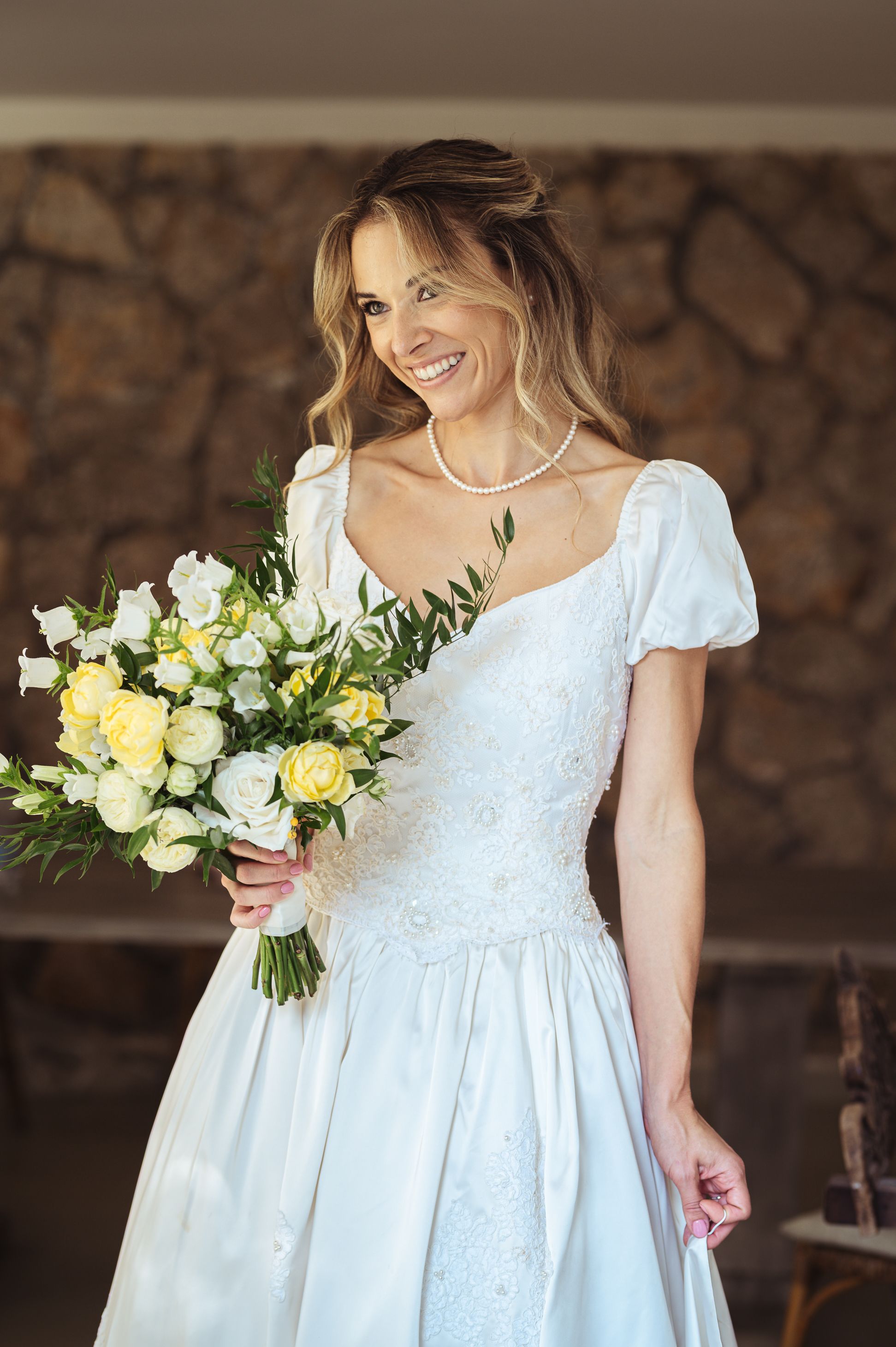 Elegant bride in puff sleeve white wedding dress holds beautiful bouquet of white and yellow roses.