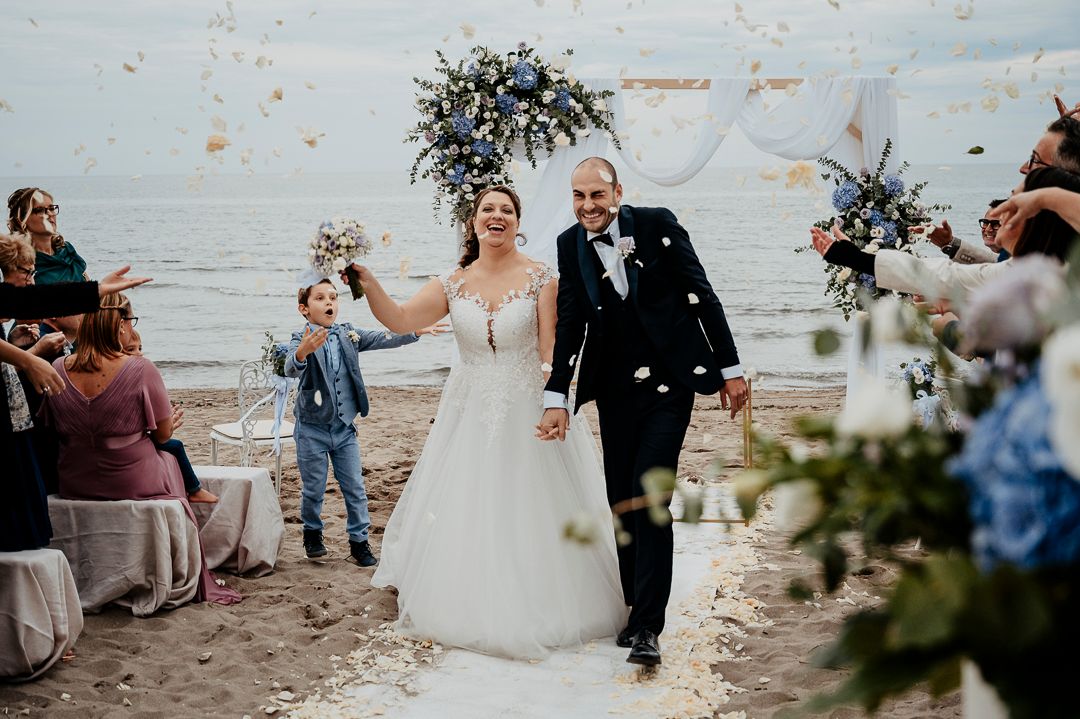 Celebratory moment with confetti being thrown on a beach during a wedding ceremony by the ocean.