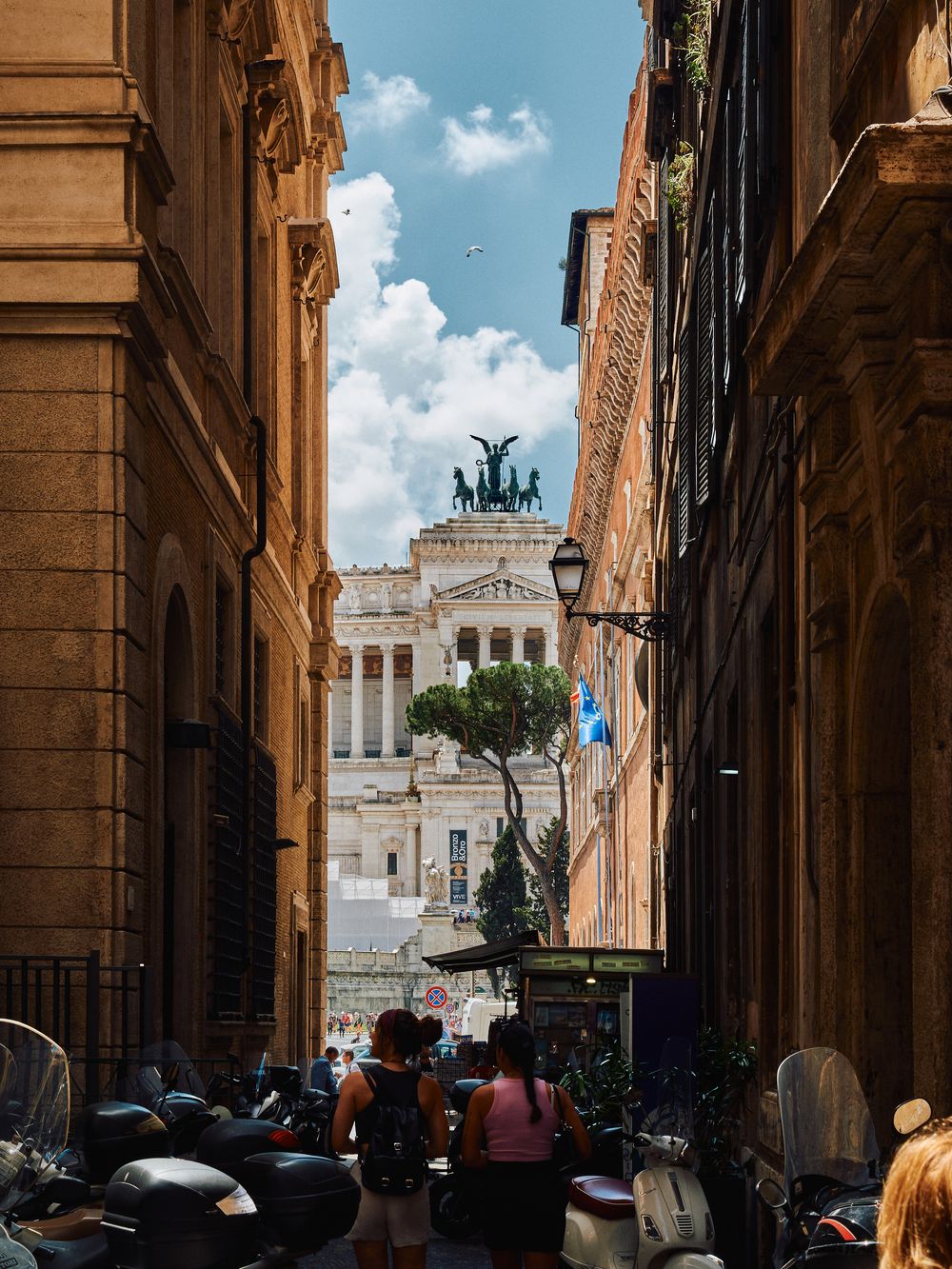 A narrow street in Rome leads to the iconic Altare della Patria monument under blue skies in progressive views.