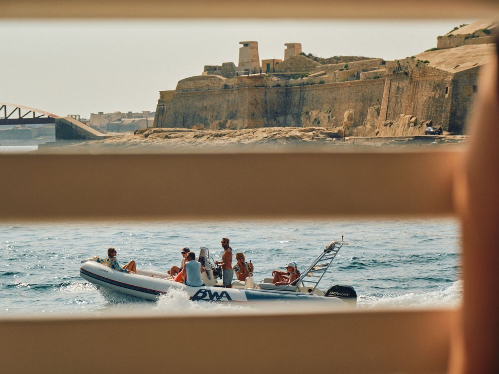 People enjoy a boat ride along the Mediterranean coast near an ancient cliff-side fortress during sunset.
