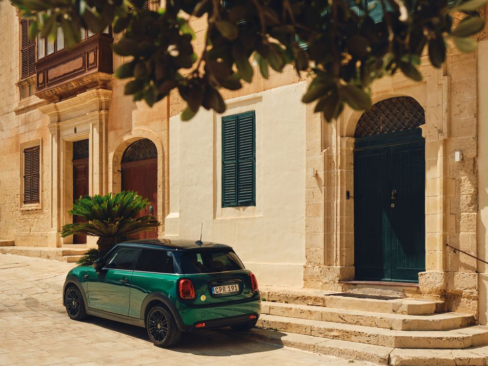 A green MINI Cooper parked in front of a Mediterranean style building with shuttered windows and stone steps.