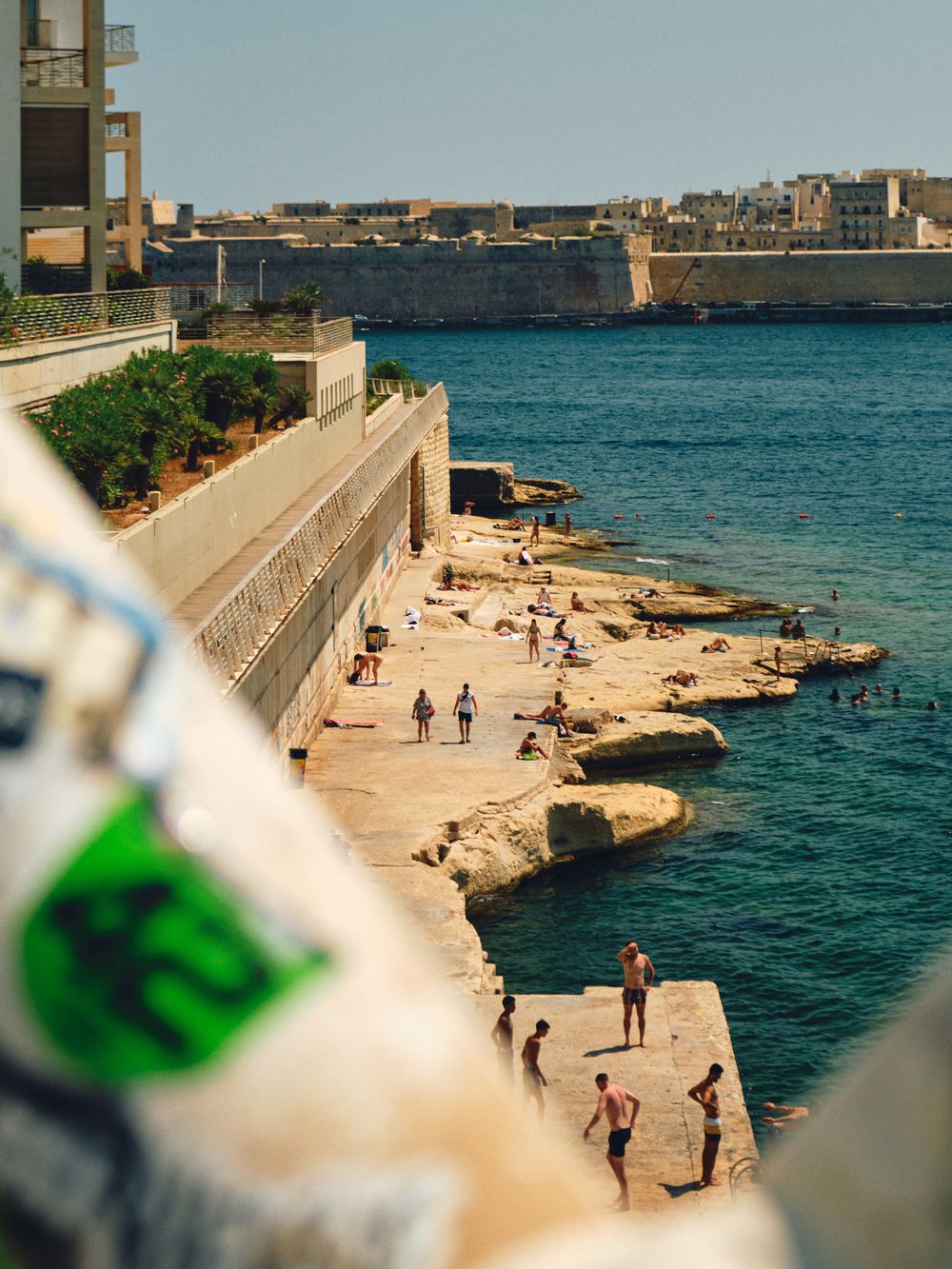 A panoramic seaside walkway with people strolling along rocky Mediterranean coast and blue waters in Valletta, Malta.
