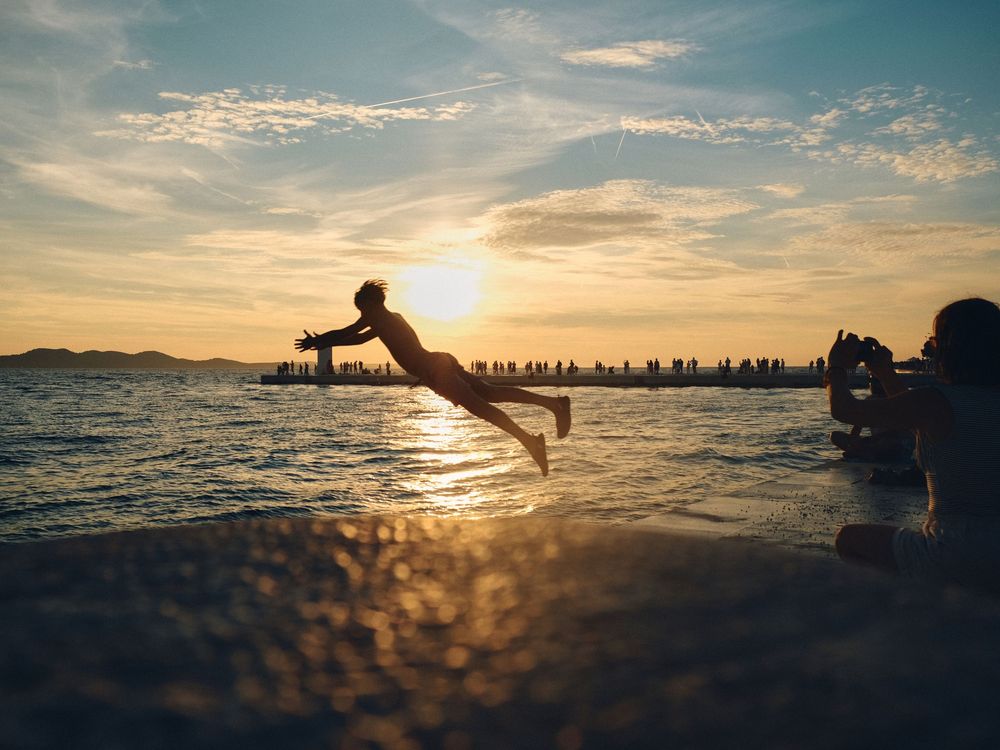 Silhouette of a person jumping into the ocean during golden sunset with pier in background.