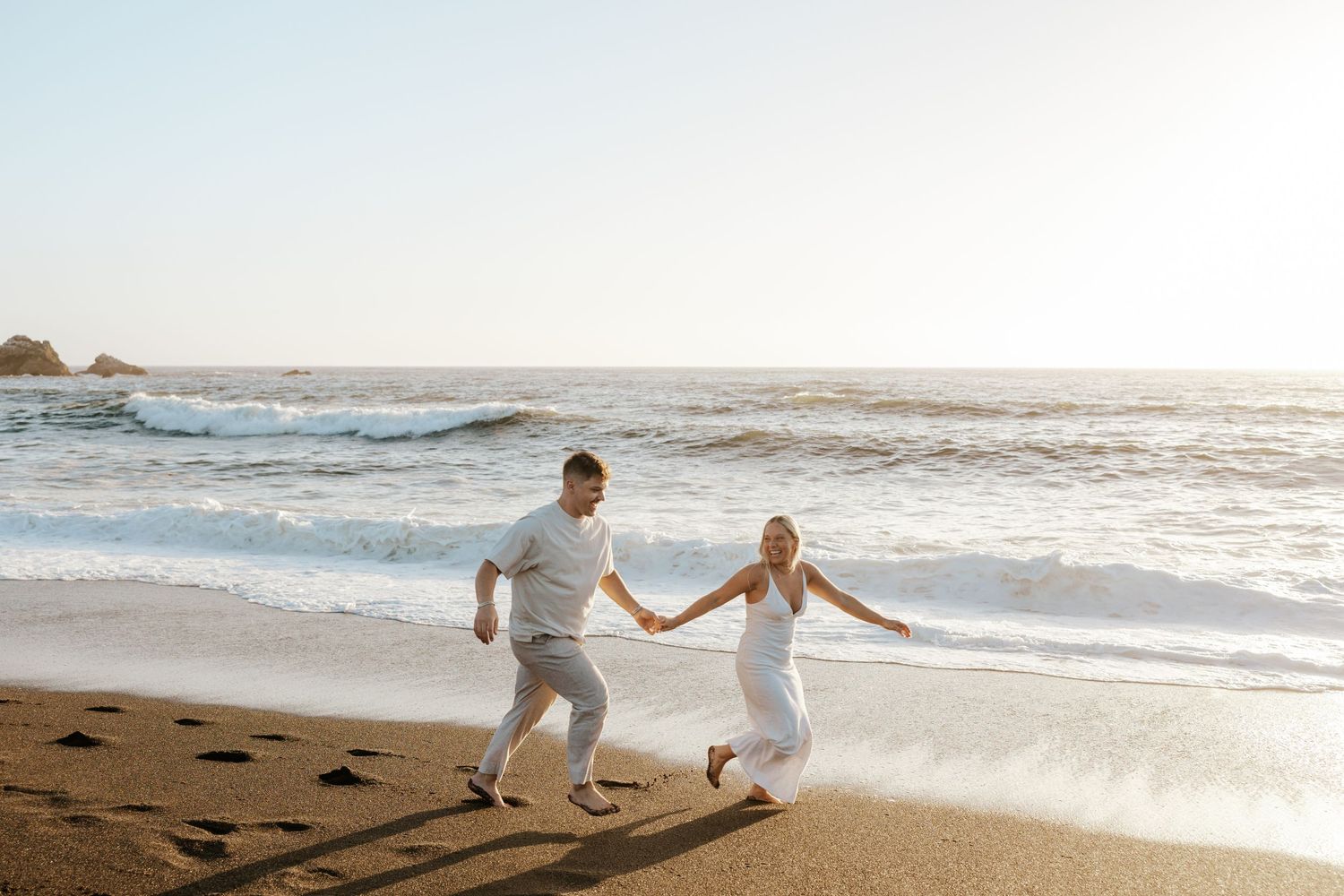 candid couple running on the beach and laughing in pacifica, near san francisco for engagement photoshoot in northern california