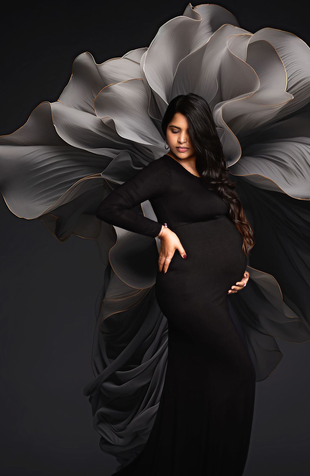 Artistic maternity photo with black gown against dramatic grey flower backdrop.