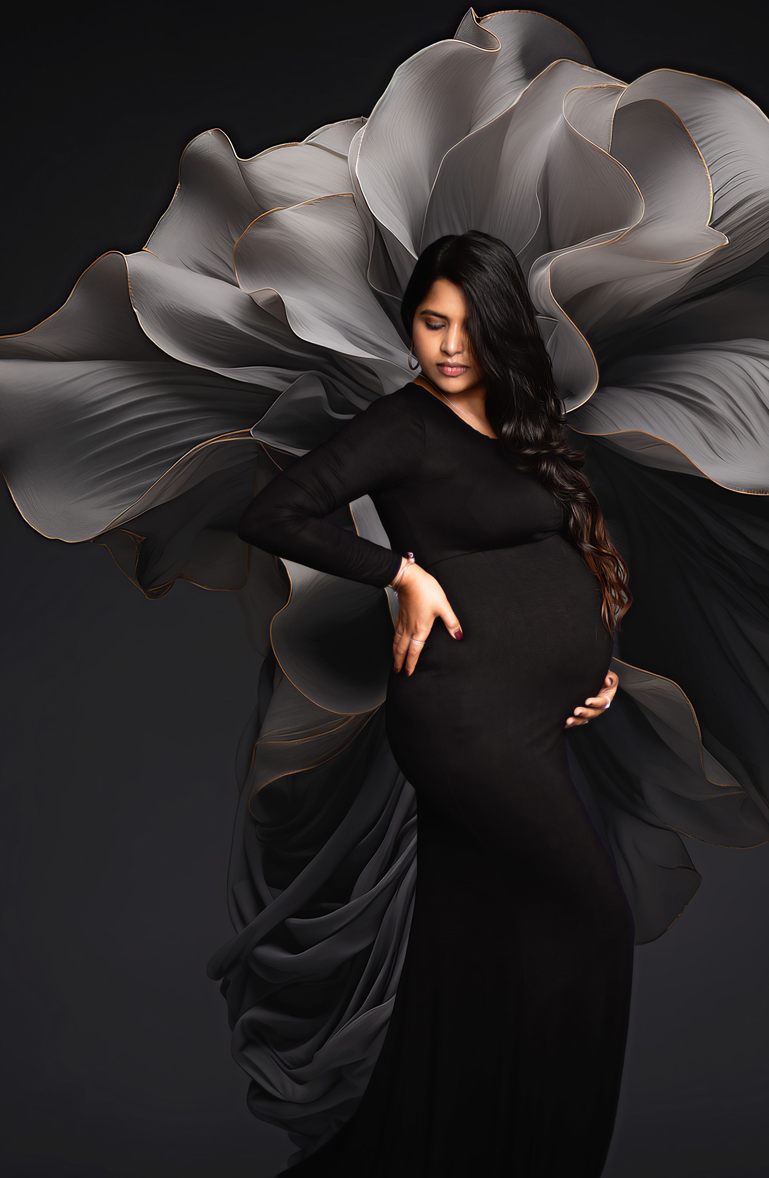 Artistic maternity photo with black gown against dramatic grey flower backdrop.