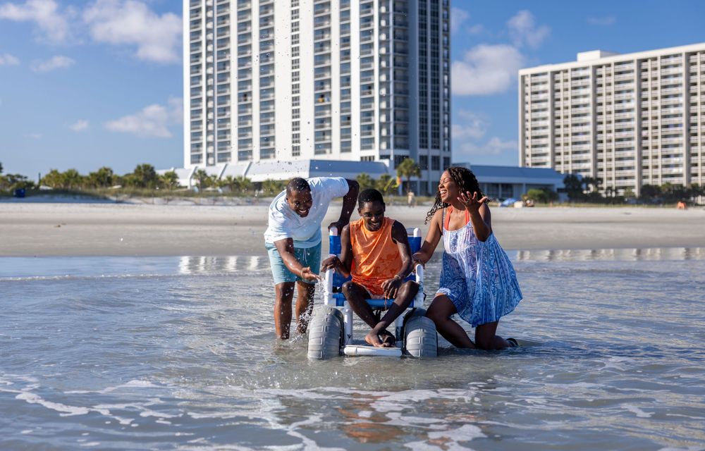Family in coordinated blue outfits posing on the Myrtle Beach shoreline. A child in a wheelchair has fun in the surf with mom and dad.