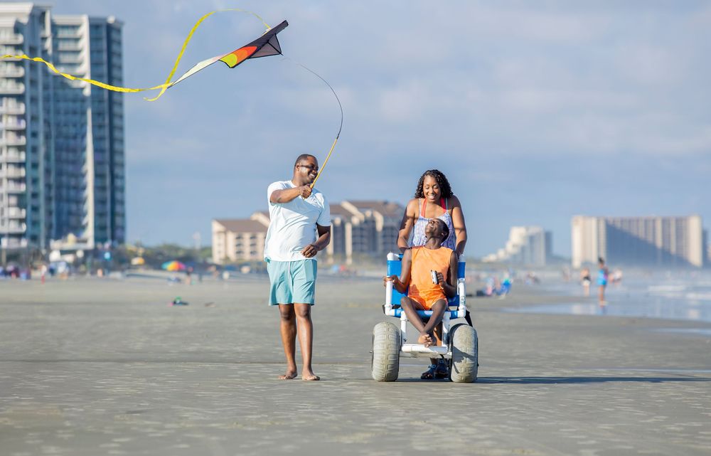 A couple flying a kite during a beach session in Myrtle Beach. A child in a wheelchair is enjoying the kite flying.
