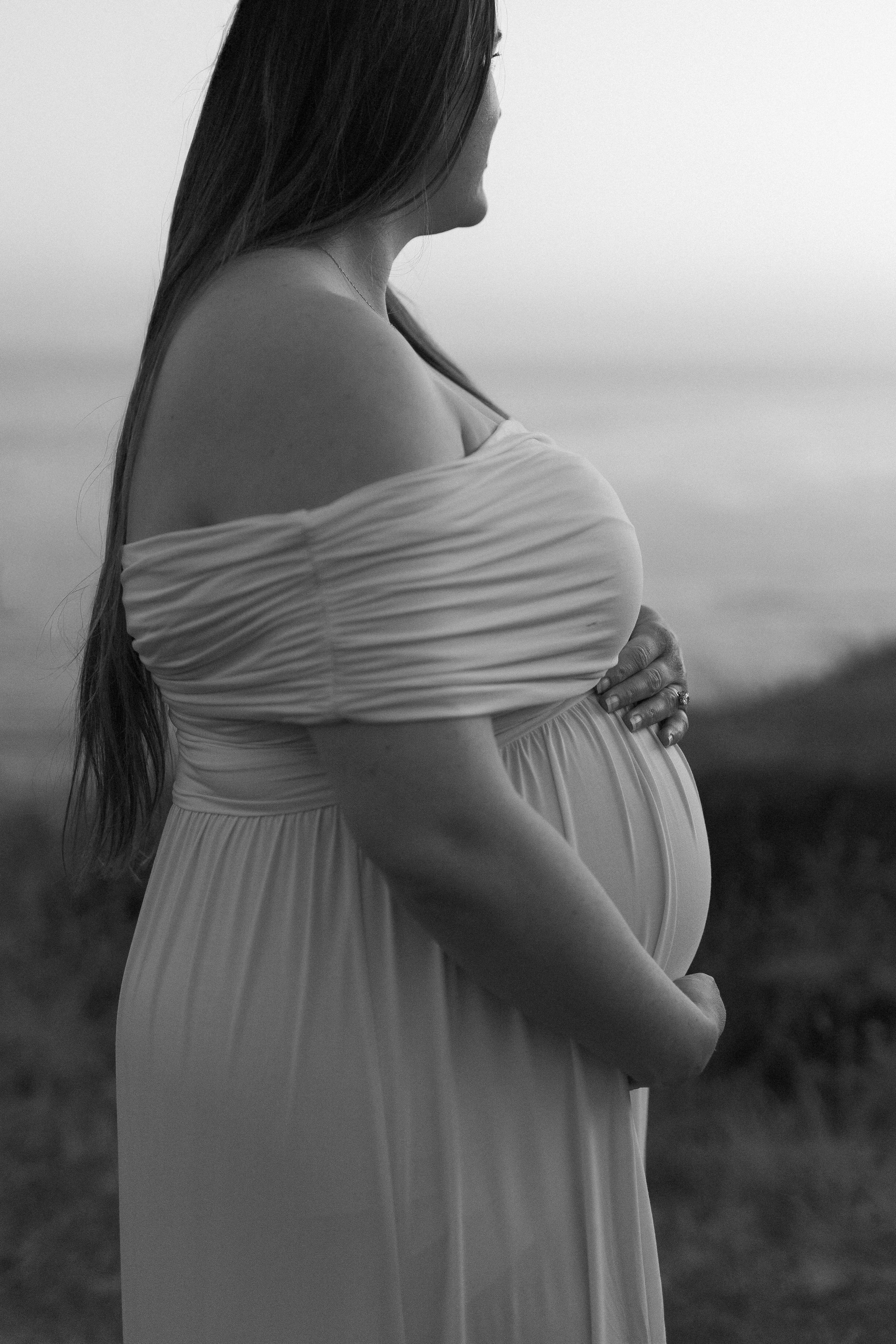 a black and white editorial photo of a woman standing on a lake for maternity photos