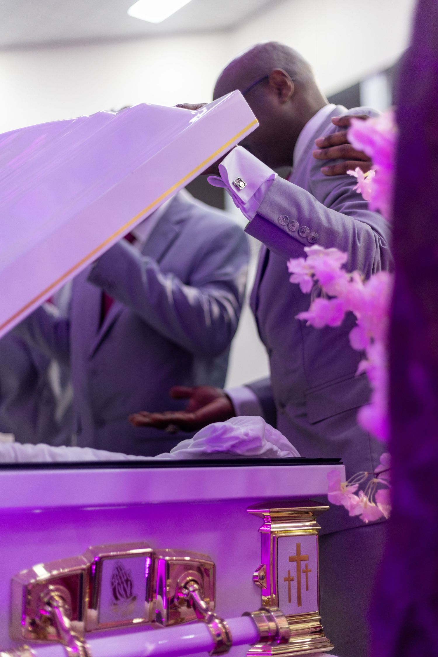 Purple-lit funeral service with casket and floral arrangements.