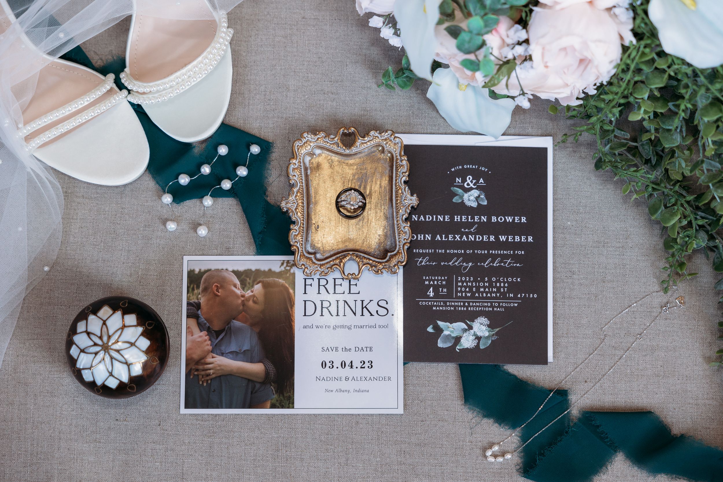 Wedding flat lay with invitation suite, bridal shoes, ring, pearls, and floral accents on a elegant styled table.