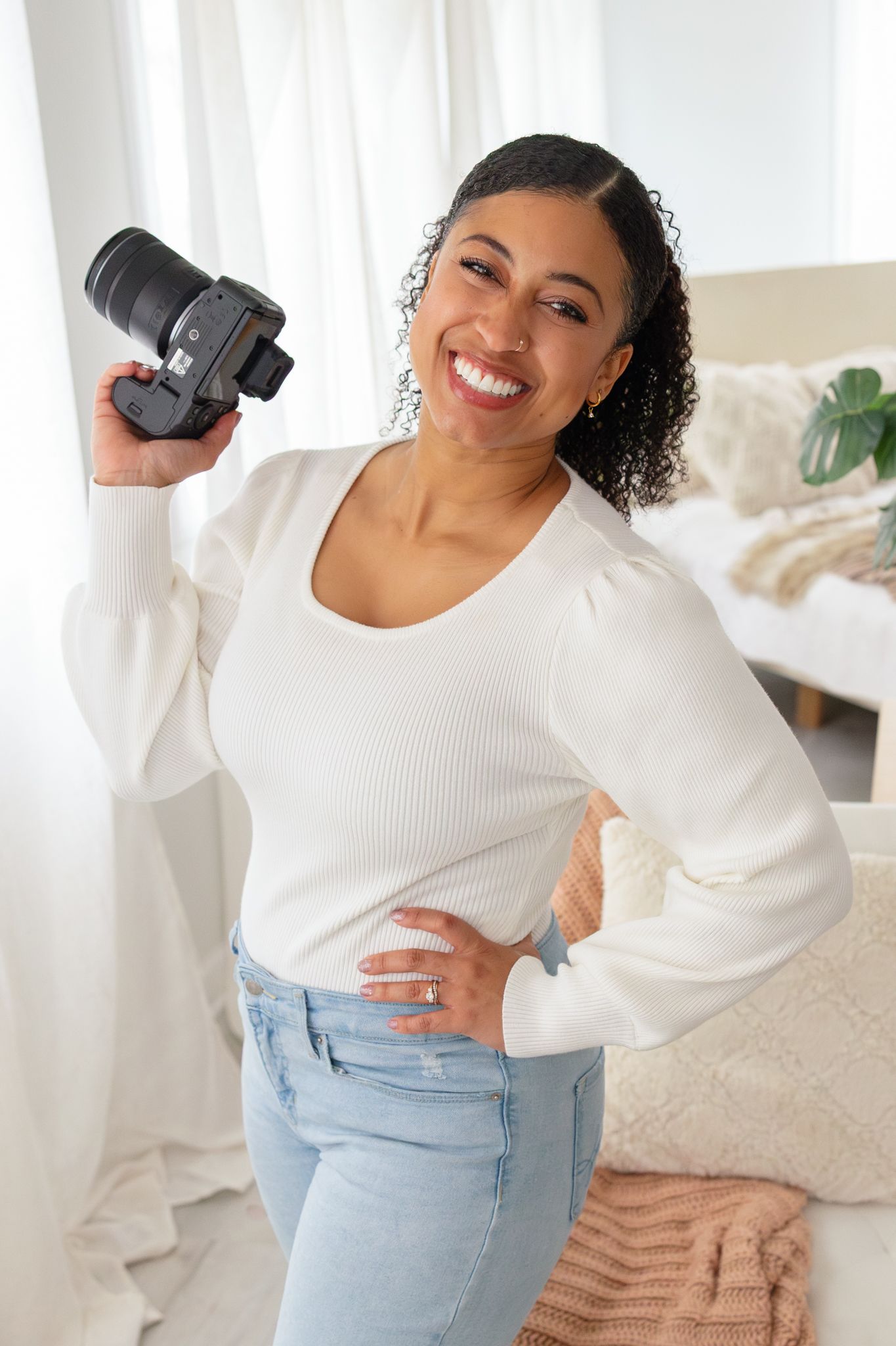 Professional photographer in black tank top poses with camera while seated in white chair.