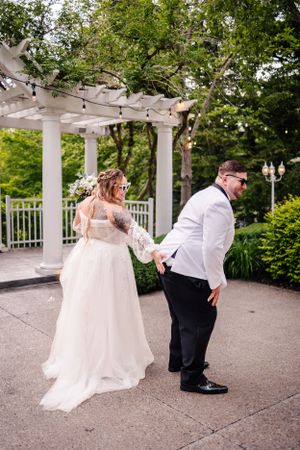 A whimsical wedding photo showing playful poses under an elegant white garden pergola.