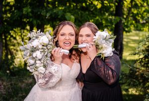 Two people playfully pose with white flower bouquets against their faces in a sunny outdoor setting.