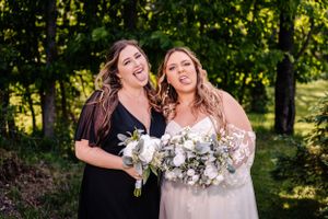 Two people pose with elegant white bouquets while making silly expressions in a forest setting.