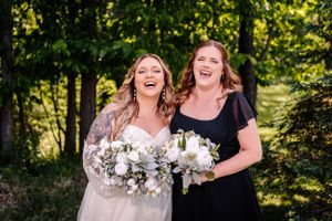 Two people laughing together while holding white floral bouquets in sunlit garden.