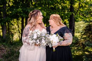 Two people sharing genuine laughter while holding elegant white bouquets outdoors.