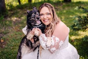 Close-up of bride with black and white dog wearing bow tie in outdoor setting.