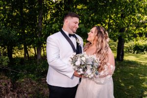 A romantic wedding portrait in a wooded setting with natural lighting and elegant floral bouquet.