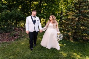 Couple walks hand in hand through sunlit garden in formal wedding attire.
