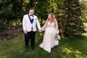 Couple holds hands while walking through lush garden setting in wedding attire.