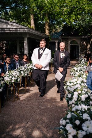 Garden pathway lined with white floral arrangements for outdoor wedding ceremony.