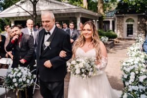 A wedding ceremony processional takes place on a flower-lined pathway.