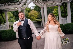 A joyful wedding couple holds hands and walks beneath an outdoor pergola structure.