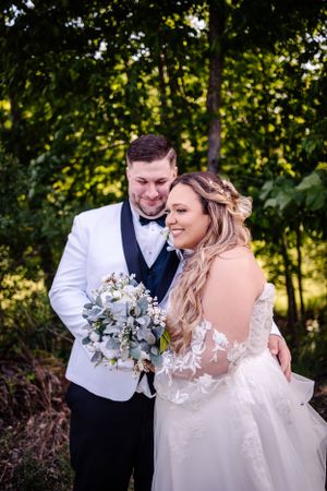 A couple shares an intimate moment in formal wedding attire against a lush forest backdrop.