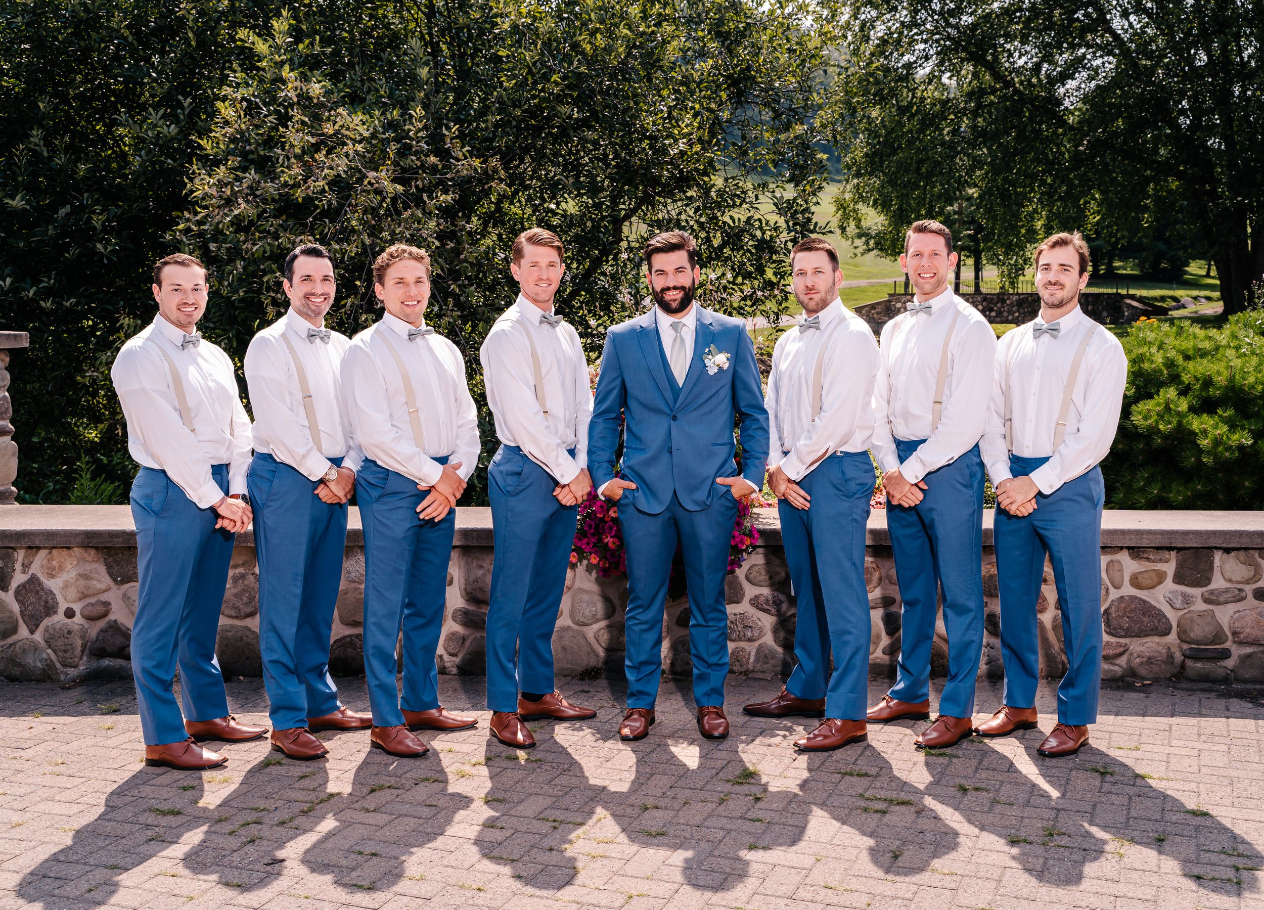 Wedding party groomsmen in blue jeans and white shirts pose with groom in blue blazer.