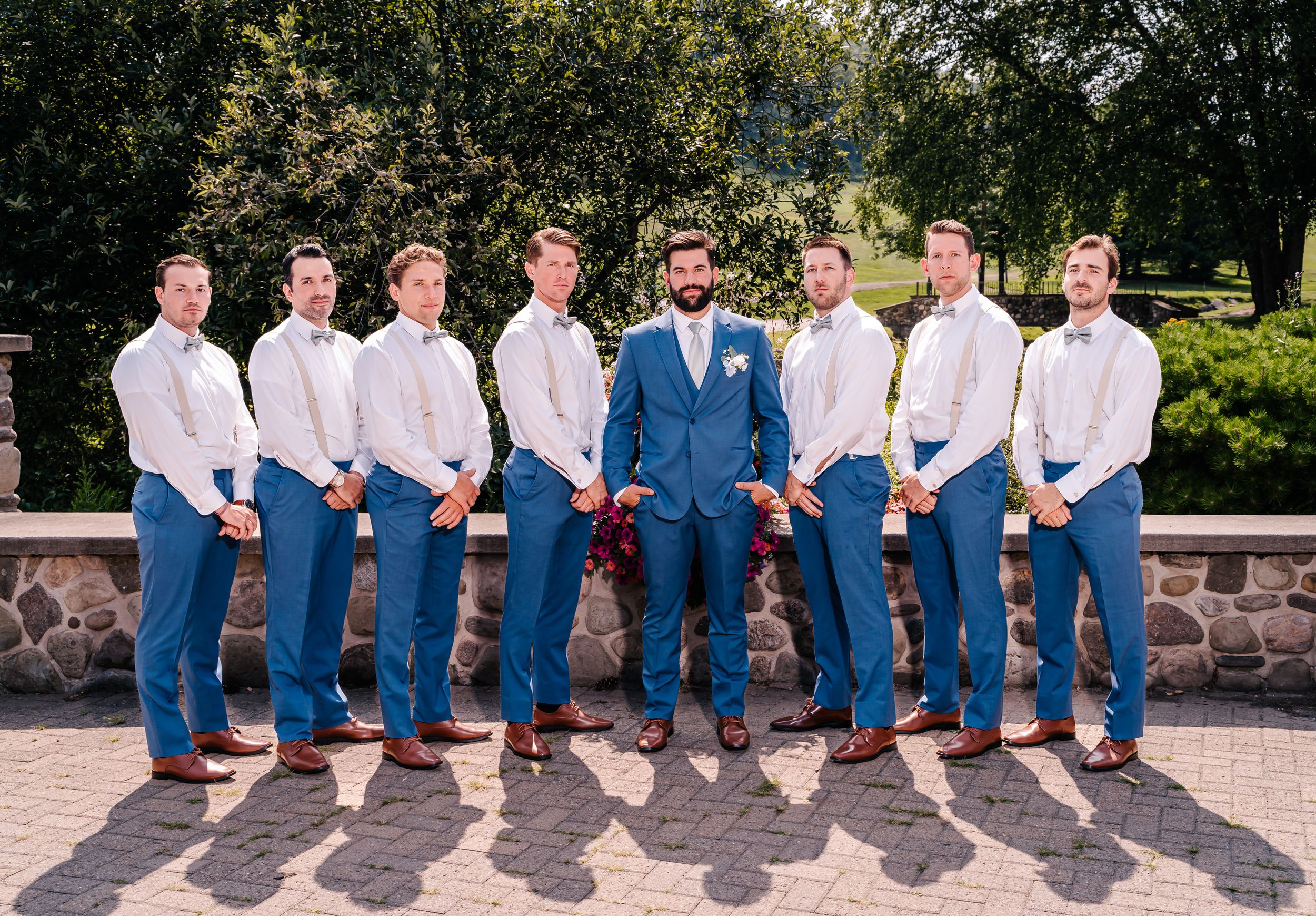Groomsmen lineup wearing coordinated white shirts and jeans with groom in blue jacket.