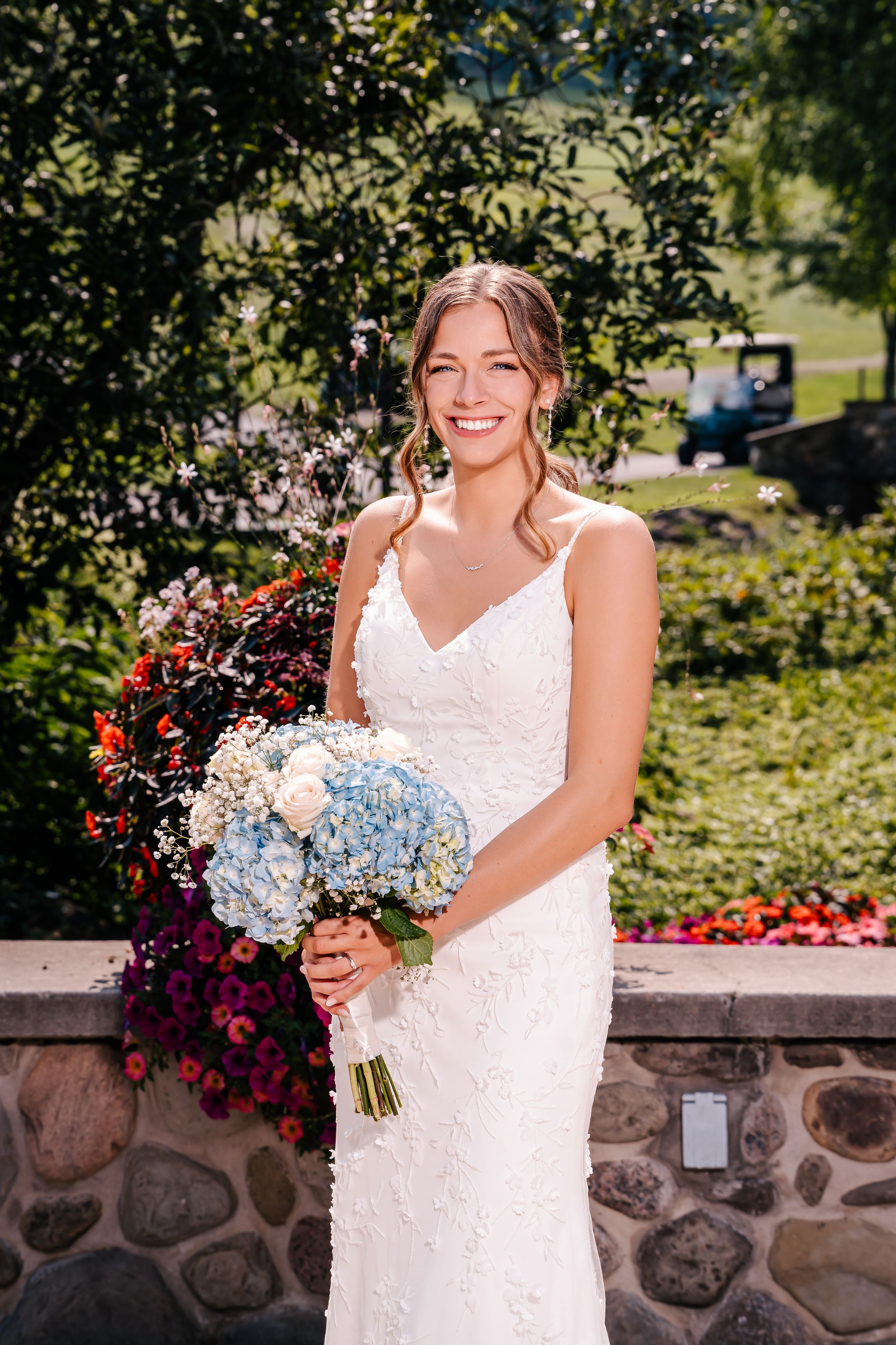 Radiant bride holding blue and white bouquet smiles in lace wedding dress outdoors.