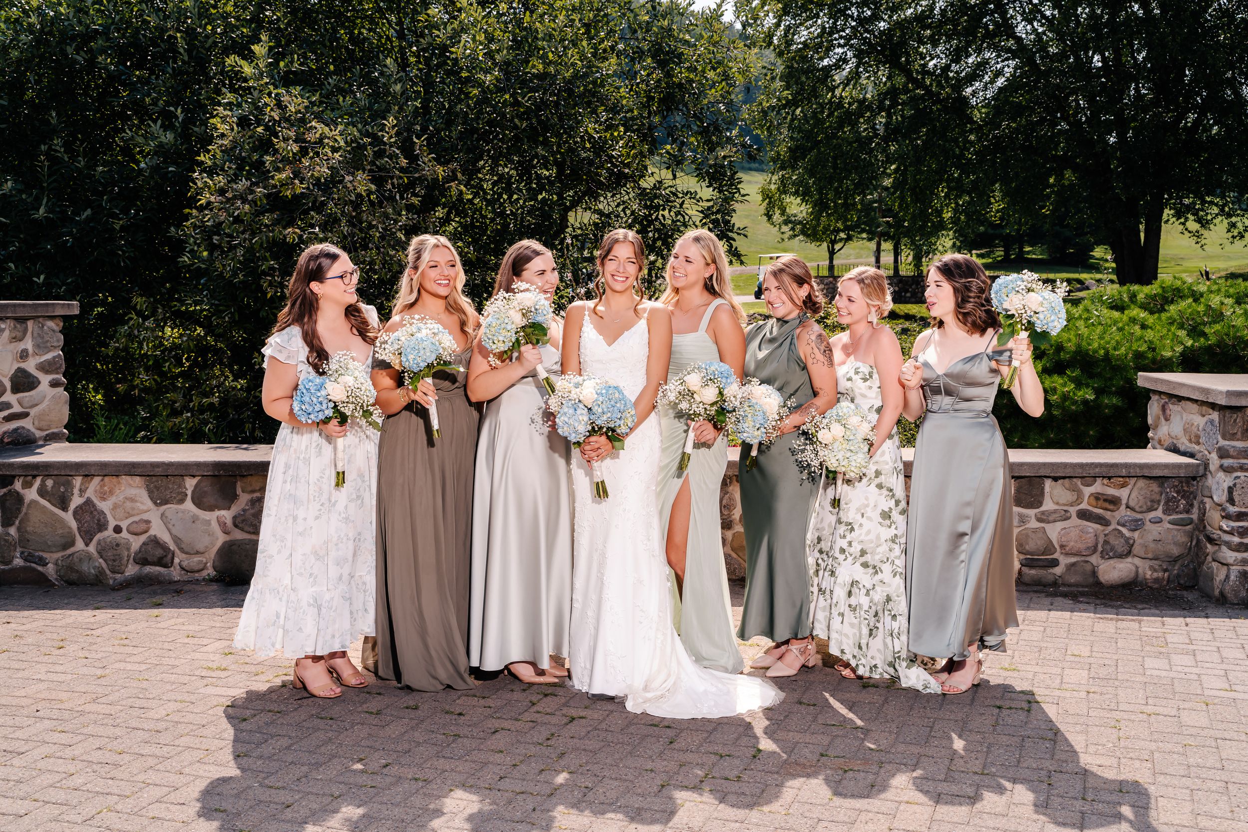 Bridal party group shot with mixed floral and solid dresses holding bouquets.