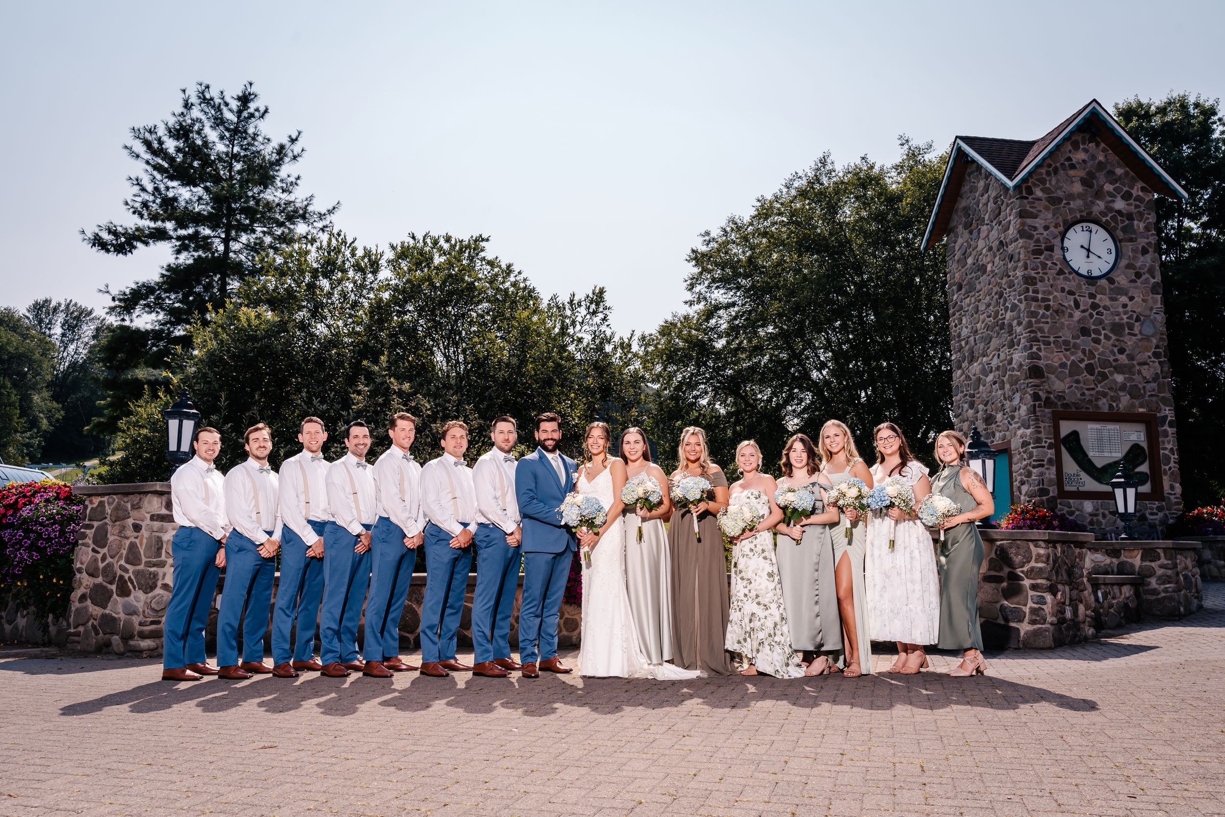 Wedding party poses in front of stone clock tower with coordinated blue and neutral attire.