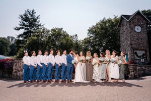 Bridal party poses outdoors with coordinated attire in front of rustic stone building.