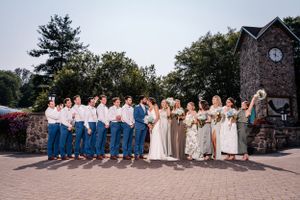 Wedding party members arranged in line wearing coordinated blue and neutral outfits near stone structure.