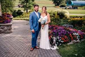 Couple poses in formal attire amid colorful flower garden with mountain backdrop.